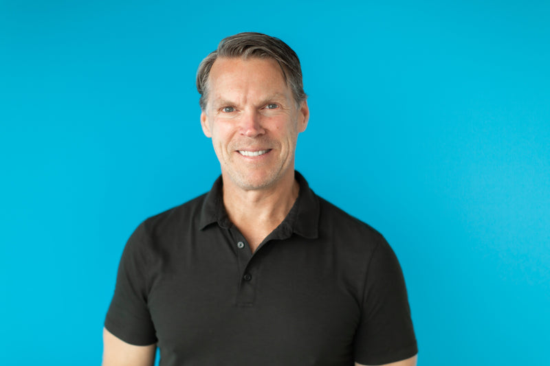 Dr. Darren Burke wearing a black polo shirt against a blue background